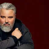 Mirosław Niewiadomski, z siwą brodą i włosami, w bluzie z kapturem. Jego życiorys to historia pasji i determinacji.