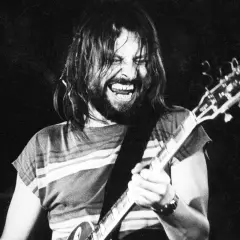 Rockman z długimi włosami i brodą, grający na gitarze z pasją. Jego twarz wyraża emocje, jakby to była jego osobista dżem modlitwa.