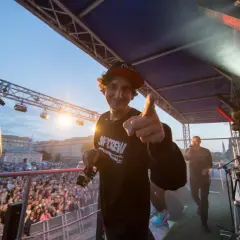 Kosi z JWP Crew w wieku około 30 lat, na scenie z mikrofonem, wskazuje palcem na widownię.