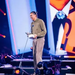 Stromae z nagrodą na scenie, jakby śpiewał "Papaoutai tekst po polsku".