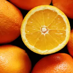 W pustej szklance pomarańcze, jedna przekrojona na pół, otoczona innymi całymi owocami.