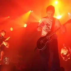 Koncert Myslovitz. Wokalista i gitarzysta na scenie, w tle basista. Czerwone światła podkreślają energię utworów.
