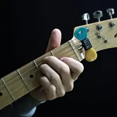 Dłoń grająca akord na gryfie gitary Fender Telecaster. Kostka z uchwytem na gryfie.