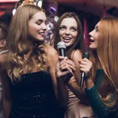 Trzy kobiety śpiewają do mikrofonów, bawiąc się przy fajnych piosenkach do śpiewania.