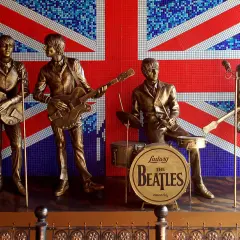 Brązowe posągi **The Beatles** grające na tle mozaikowej flagi Wielkiej Brytanii.