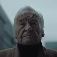 Twarz starszego mężczyzny z siwymi włosami, w beżowym płaszczu. To jego mori interpretacja, jakby patrzył w przyszłość.