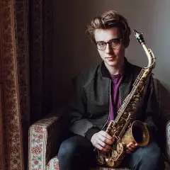 Młody muzyk z saksofonem, przyszłość najwybitniejszych polskich muzyków jazzowych, siedzi w fotelu.