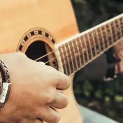 Dłoń z bransoletką gra akord d na gitarze akustycznej.