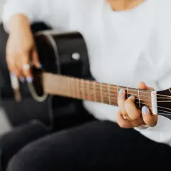 Dłoń z niebieskim lakierem na paznokciach gra akord F na gitarze.