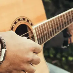 Dłoń z bransoletką gra akord C na gitarze akustycznej.
