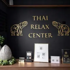 Recepcja centrum masażu tajskiego. Złote słonie i napis "THAI RELAX CENTER" na czarnej ścianie. Na blacie dekoracje i cennik. Tu możesz się wyciszyć.