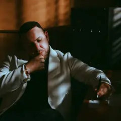 Mężczyzna w białej marynarce, Louis Villain, w zamyśleniu. Jego wiek nie jest widoczny, ale jego postawa sugeruje dojrzałość.