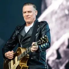 Bryan Adams w skórzanej kurtce gra na gitarze, przypominając klimat lata '69.