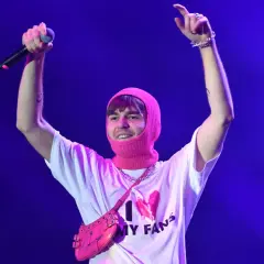 Artysta w różowej kominiarce i koszulce "I ❤️ MY FANS" z torebką na ramię, z mikrofonem w dłoni, pozdrawia publiczność.