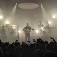 Koncertowy wokalista z gitarą, otoczony dymem i światłami. Publiczność wznosi telefony, wołając "nie zapomnij mnie".