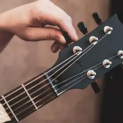 Dłoń kręci kluczem przy główce gitary, by ustawić struny w standard tuning.