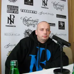 Peja w czarnej bluzie z niebieskim logo, przed mikrofonem. Na ścianie za nim napisy: "TERRORYM", "REEDUKACJA", "Definicja Peja". Wiecie co z nim zrobić.