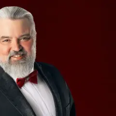 Mirosław Niewiadomski, tenor, w czarnym smokingu z czerwoną muszką, uśmiecha się do widza.