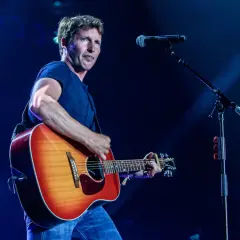 James Blunt na koncercie, grając na gitarze. W tle mikrofon, przypominający o jego hicie "You're Beautiful".