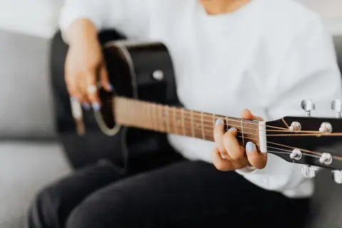 Dłoń z niebieskim lakierem na paznokciach gra akord F na gitarze.