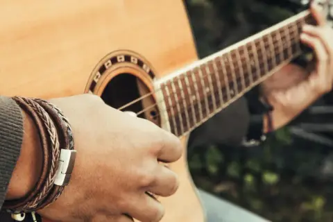 Dłoń grająca na gitarze, tworząca akord e moll. Na nadgarstku widać bransoletkę ze skóry.