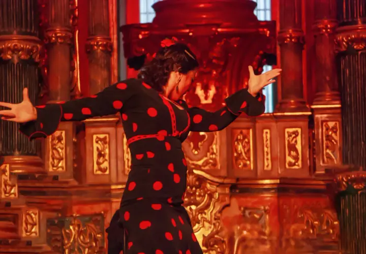 Tancerka flamenco w czarnej sukience w czerwone grochy, pełna **allegria**, porusza się na tle bogato zdobionej, złotej sceny.