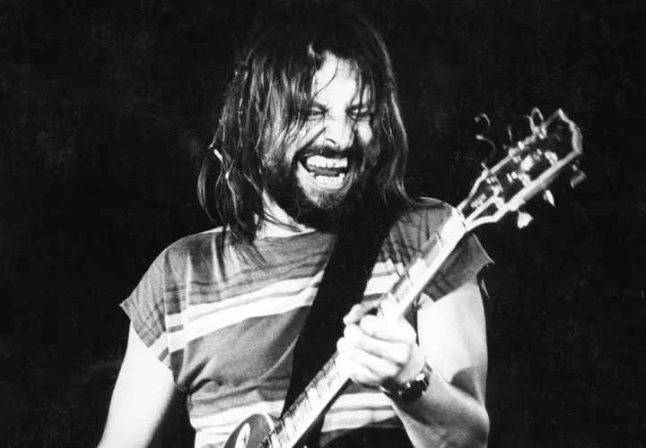 Rockman z długimi włosami i brodą, grający na gitarze z pasją. Jego twarz wyraża emocje, jakby to była jego osobista dżem modlitwa.