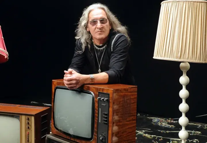 Mężczyzna z długimi siwymi włosami i okularami opiera się o stary telewizor. Wokół niego lampy i inne telewizory. Widać, że trzeba wiedzieć, kiedy ze sceny zejść.