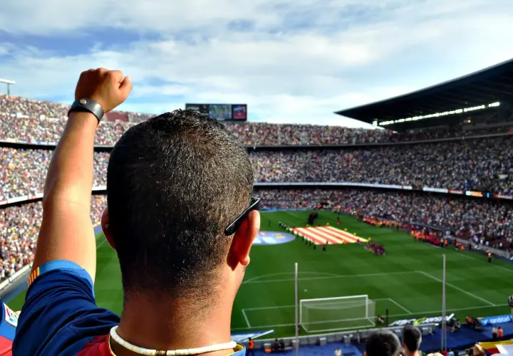 Widok z trybun stadionu na murawę, gdzie kibice tworzą mozaikę z flag, a w tle słychać hymn Barcelony.