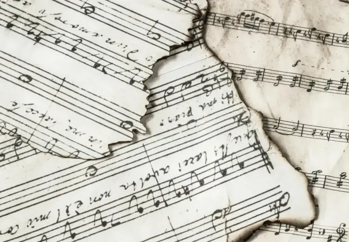 Spalone nuty z zapisem muzycznym, gdzie widać nuty i tekst. Wśród nich odnaleźć można znak bemol w muzyce, świadczący o obniżeniu dźwięku.