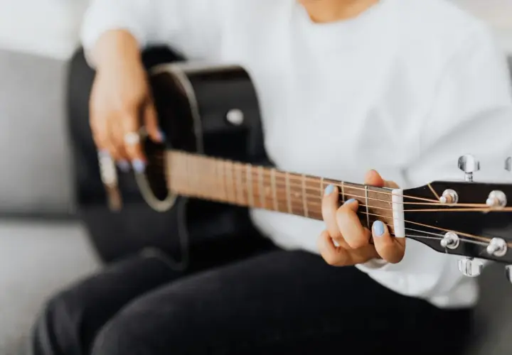 Dłoń z niebieskim lakierem na paznokciach gra akord F na gitarze.