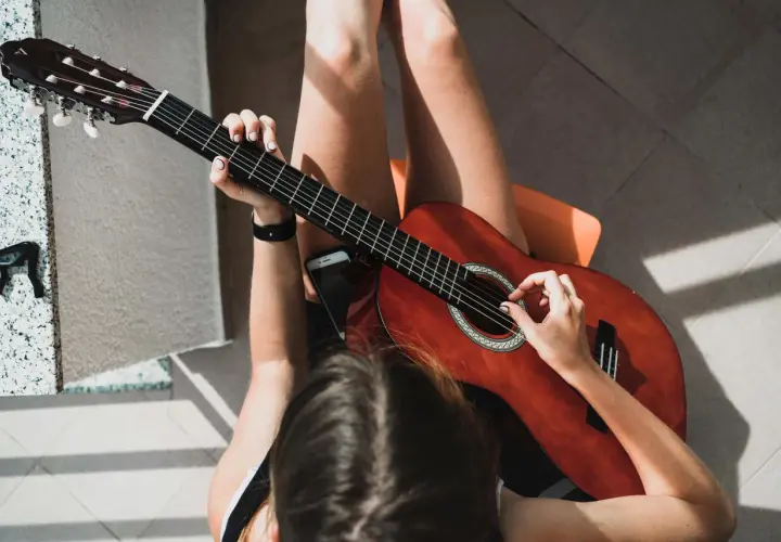 Dziewczyna gra na gitarze, jej palce tworzą akord g. Słońce rzuca ciekawe cienie.