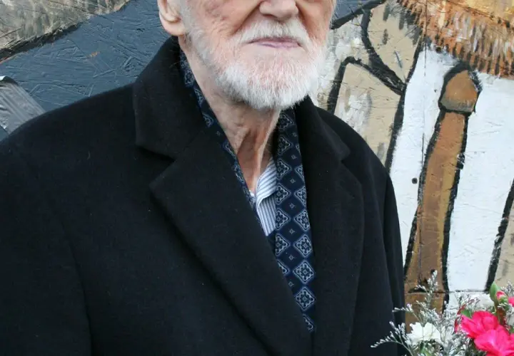 Starszy pan z siwą brodą, elegancko ubrany w czarny płaszcz i wzorzystą apaszkę, to legendarny walicki muzyk jazzowy.