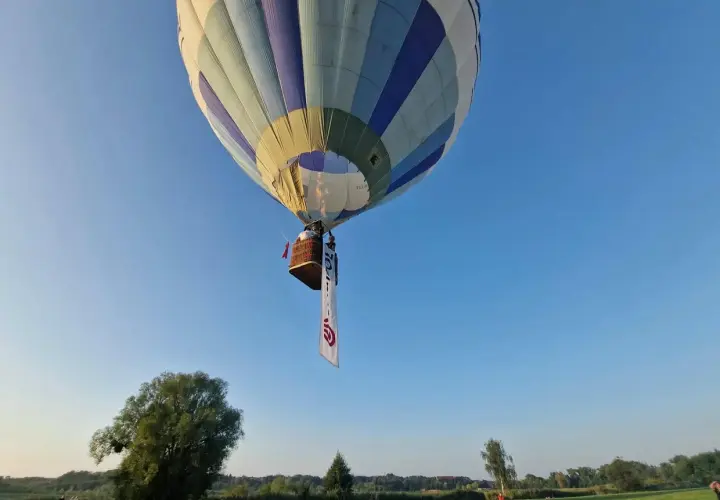Balon z koszem i banerem unosi się na błękitnym niebie. Może to symbolizować wolność, jak w piosence "99 luftballons znaczenie".