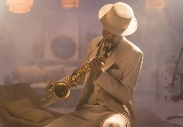 Mężczyzna w eleganckim garniturze i kapeluszu gra na saksofonie, tworząc niepowtarzalny styl w muzyce jazzowej.