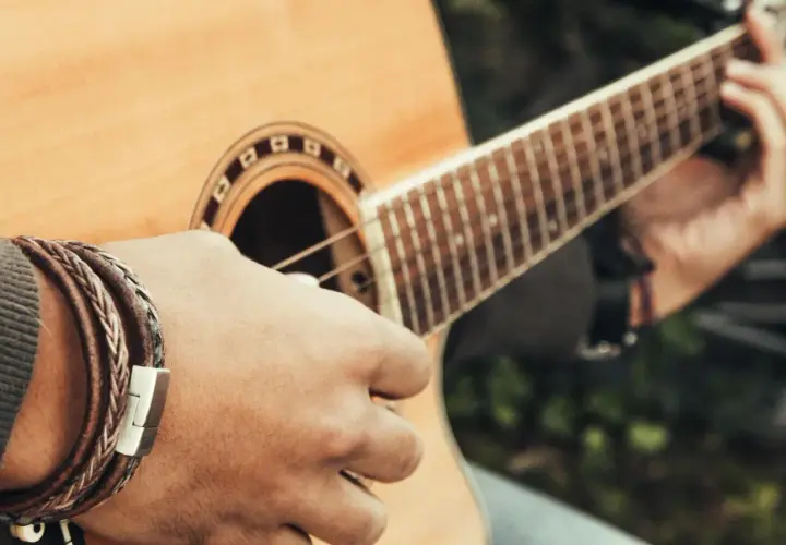 Dłoń grająca na gitarze, tworząca akord e moll. Na nadgarstku widać bransoletkę ze skóry.