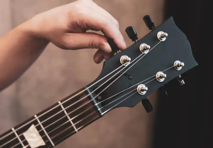 Dłoń kręci kluczem przy główce gitary, by ustawić struny w standard tuning.