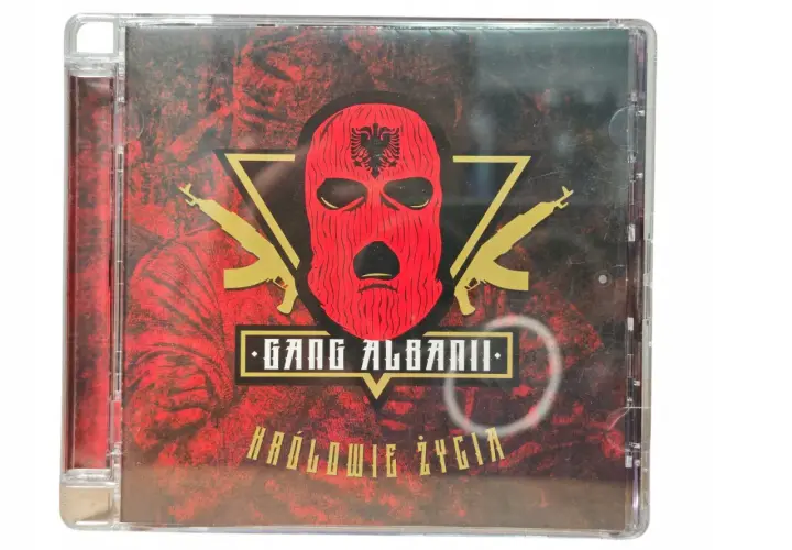 Okładka płyty CD "Królowie życia" zespołu Gang Albanii. Czerwona kominiarka z orłem, złote kałasznikowy i mroczne tło.