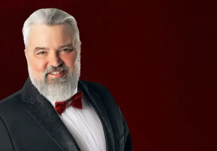 Mirosław Niewiadomski, tenor, w czarnym smokingu z czerwoną muszką, uśmiecha się do widza.