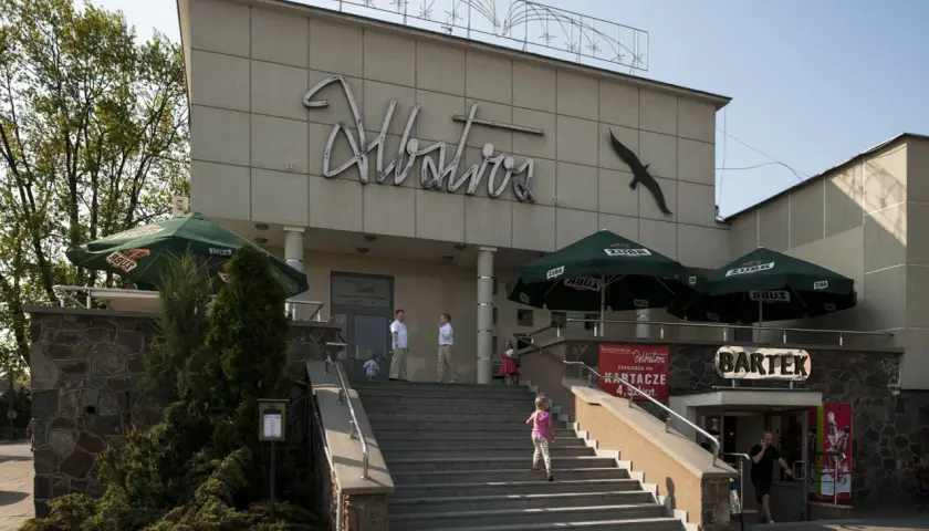 Budynek z napisem "Albatros" i sylwetką ptaka. Na schodach widać siedem dziewcząt z albatrosa, bawiących się w upalny dzień.