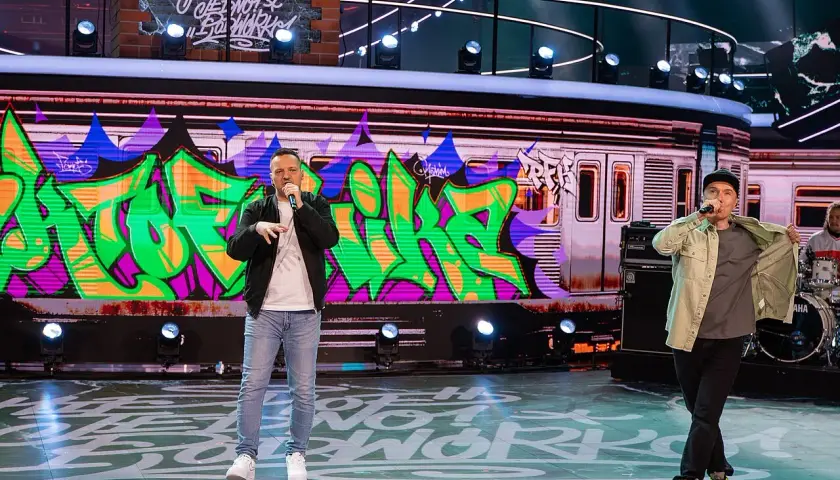 Raperzy na scenie, w tle graffiti na wagonie metra. To scena z koncertu, gdzie brzmią **paktofonika utwory**.