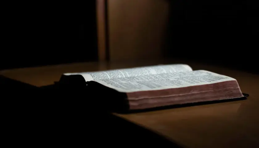 Otwarta Biblia na drewnianym stole, światło pada na strony. Słowa mądrości trwają, dopóki ziemia kręci się.