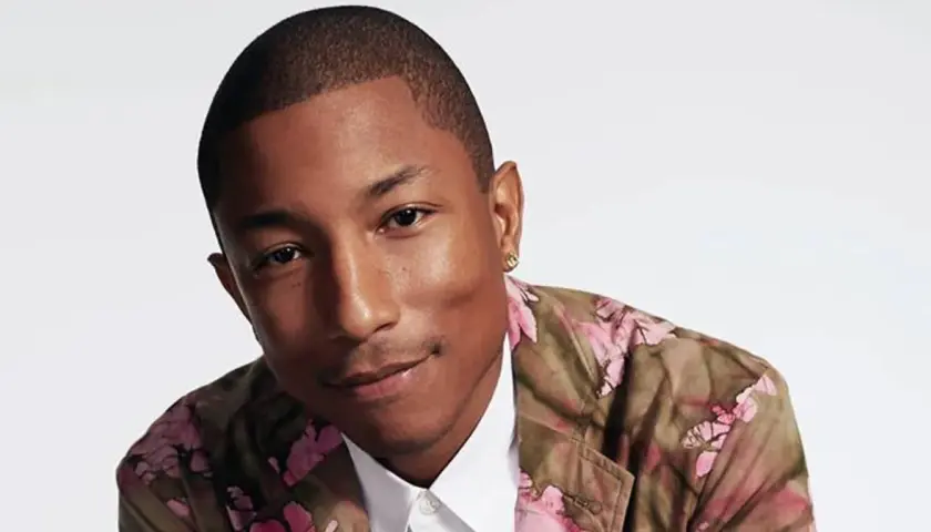 Pharrell Williams w kwiecistej marynarce, uśmiecha się, emanując pozytywną energią, jak w tekście "Happy".