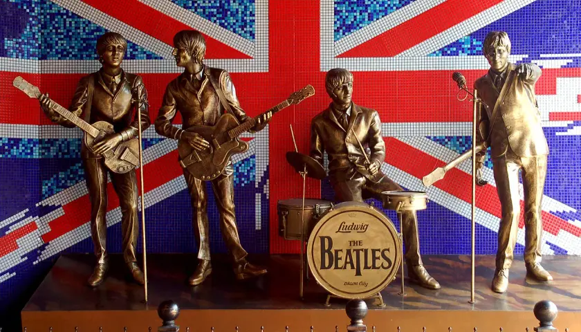 Brązowe posągi **The Beatles** grające na tle mozaikowej flagi Wielkiej Brytanii.