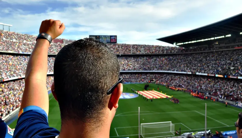 Widok z trybun stadionu na murawę, gdzie kibice tworzą mozaikę z flag, a w tle słychać hymn Barcelony.