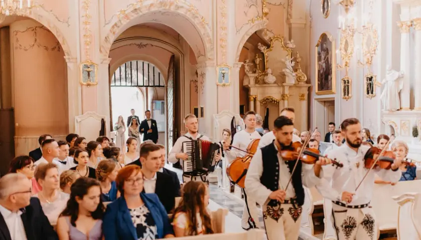 Muzycy grają pieśń na wejście w kościele. W tle para młoda wchodzi do świątyni.