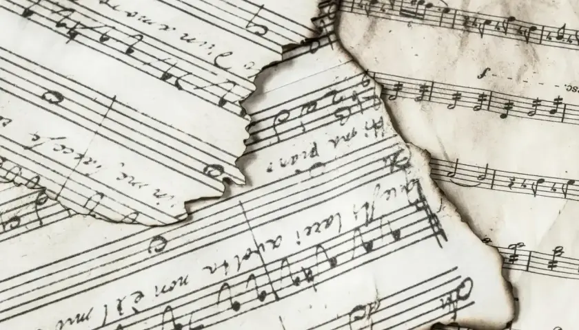 Spalone nuty z zapisem muzycznym, gdzie widać nuty i tekst. Wśród nich odnaleźć można znak bemol w muzyce, świadczący o obniżeniu dźwięku.
