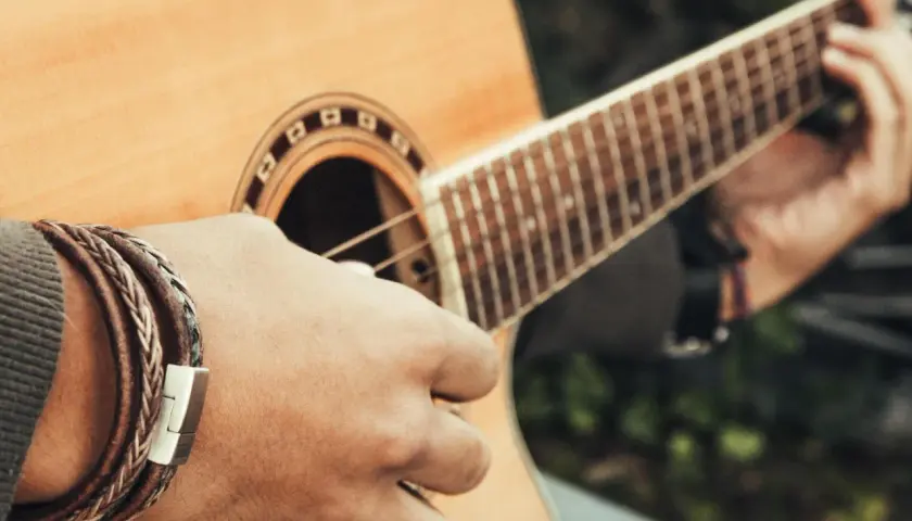 Dłoń z bransoletką gra akord d na gitarze akustycznej.