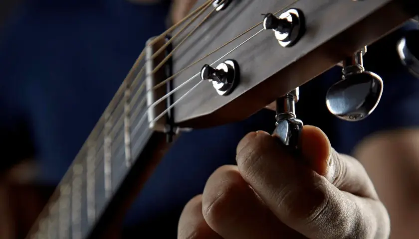 Dłoń kręci kluczem, by drop a tuning na gitarze. Idealne brzmienie jest blisko.