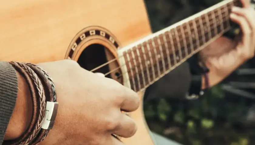 Dłoń z bransoletką gra akord C na gitarze akustycznej.